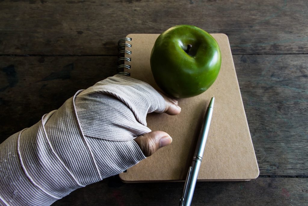 Fractured hand beside a notebook and apple
