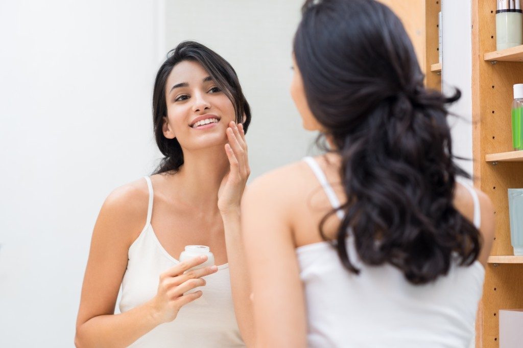 Woman caring of her beautiful skin on the face standing near mirror in the bathroom.