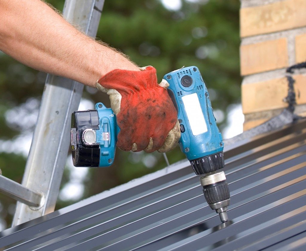 man working with a power drill on a roof