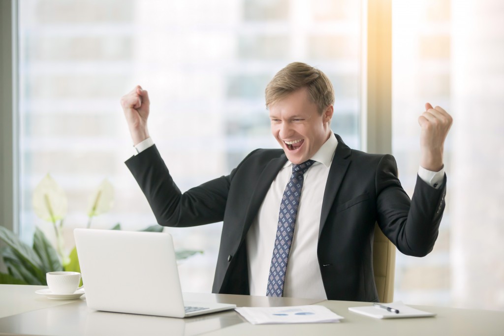 Businessman celebrating a win while looking at the laptop