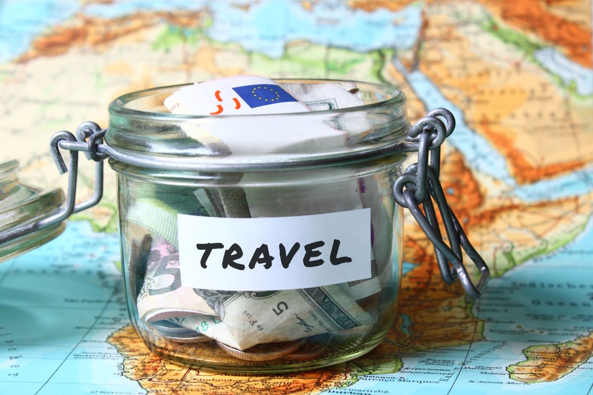 jar labeled as travel full of savings on top of a world map