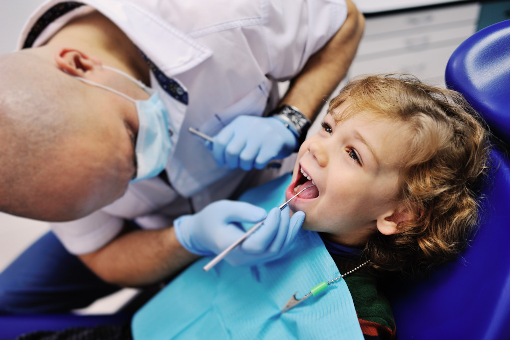 curly haired boy teeth's being checked by a dentist