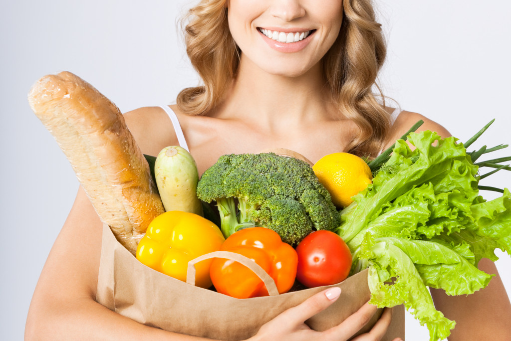 A blonde woman holding a grocery bag filled with healthy food