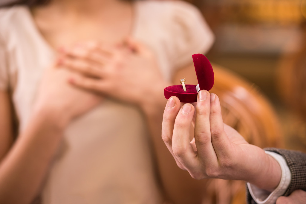 A close-up of a man presenting an engagement ring to a shocked and happy girlfriend