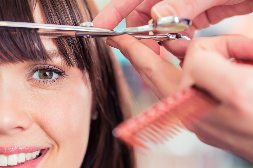 Hairdresser cutting woman's bangs in salon