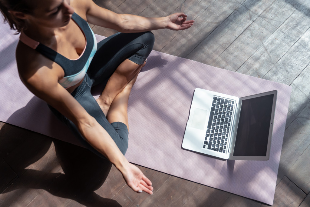 young woman doing yoga on yoga mat while online training