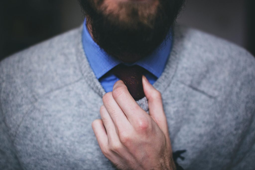 close-up of someone adjusting a necktie worn under a gray sweater