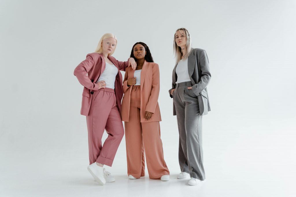 three young women in blazers, white tank tops, and sneakers posing together