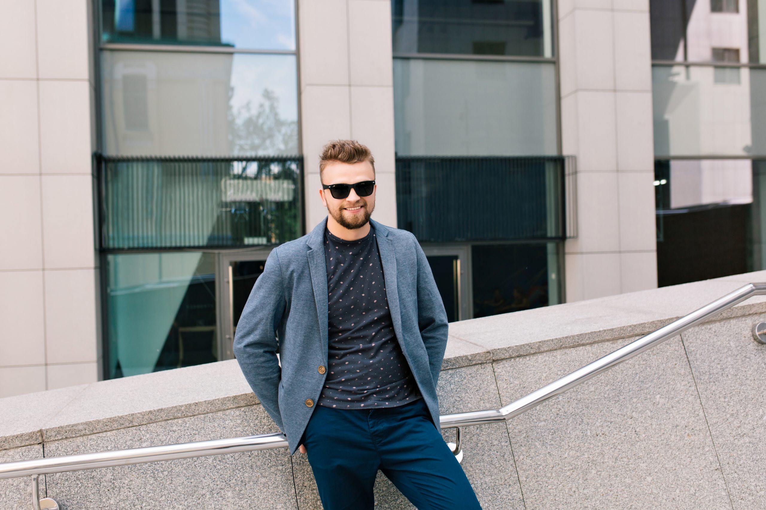 man dressed casually in jeans and a graphic shirt, paired with a blue blazer and sunglasses