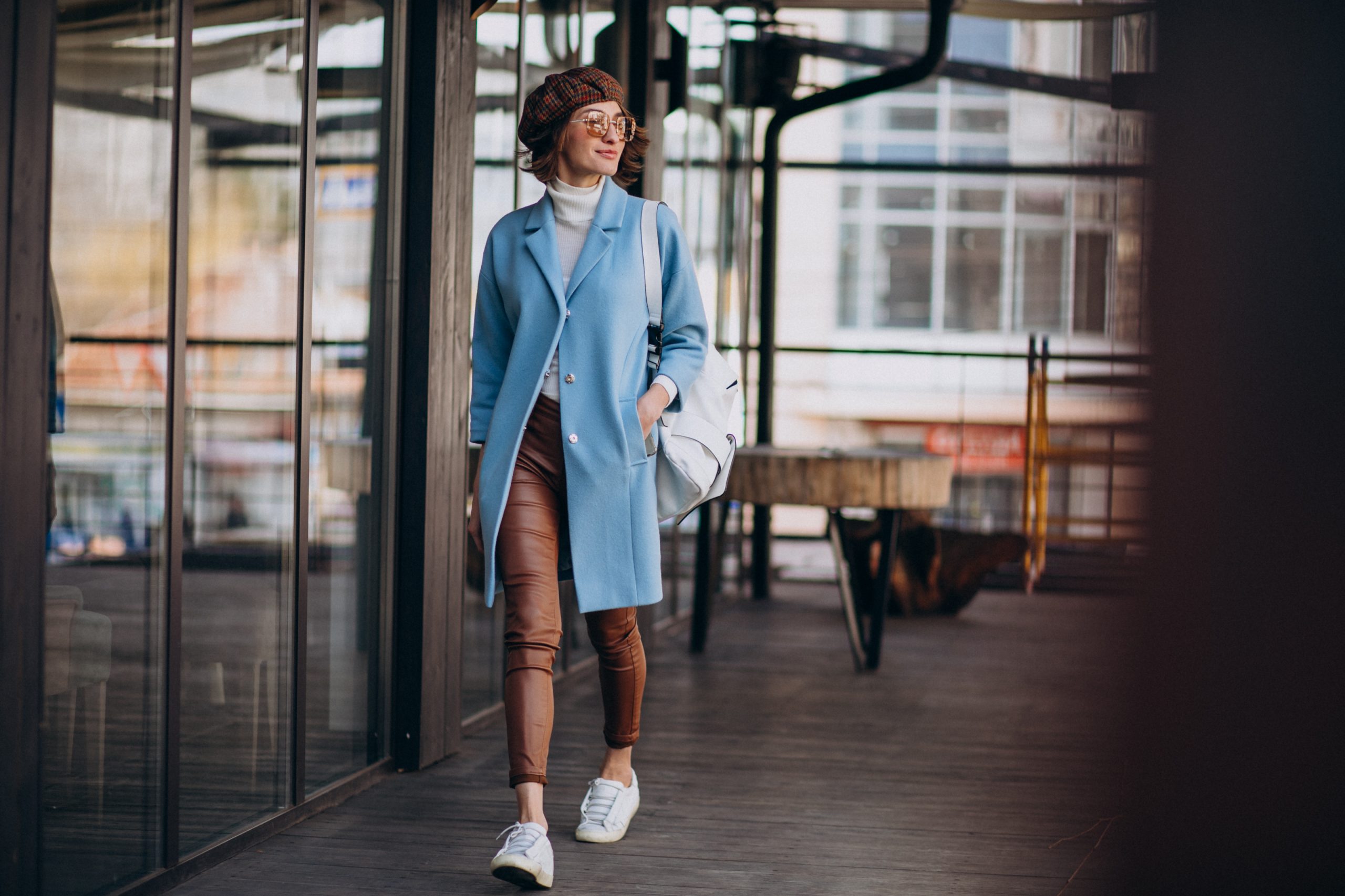 woman dressed in a powder blue coat layered over a white turtleneck, paired with brown pants and white sneakers